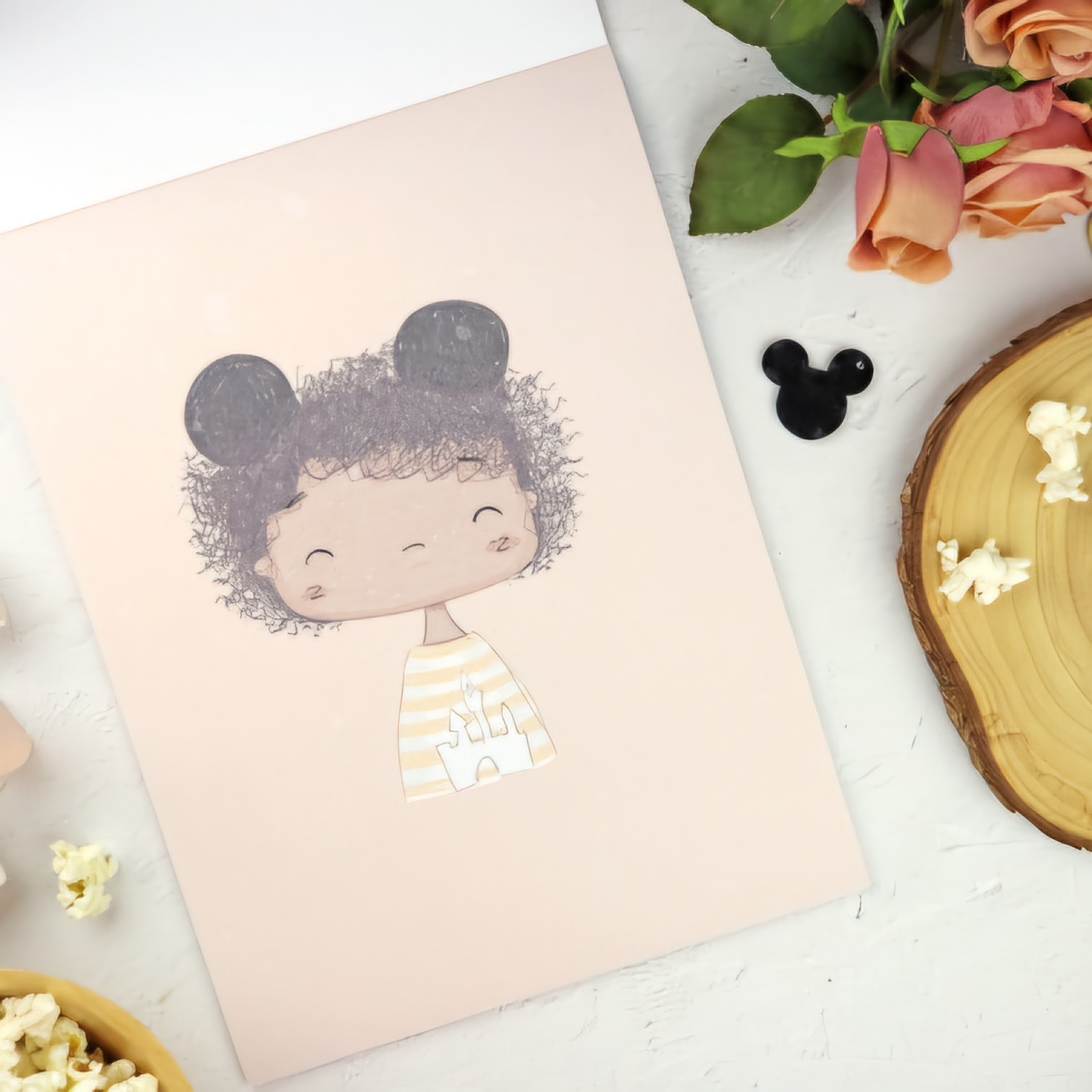 Caderno rosa com ilustração de criança e orelhas de rato, rodeado por flores, madeira, pipocas e objeto preto