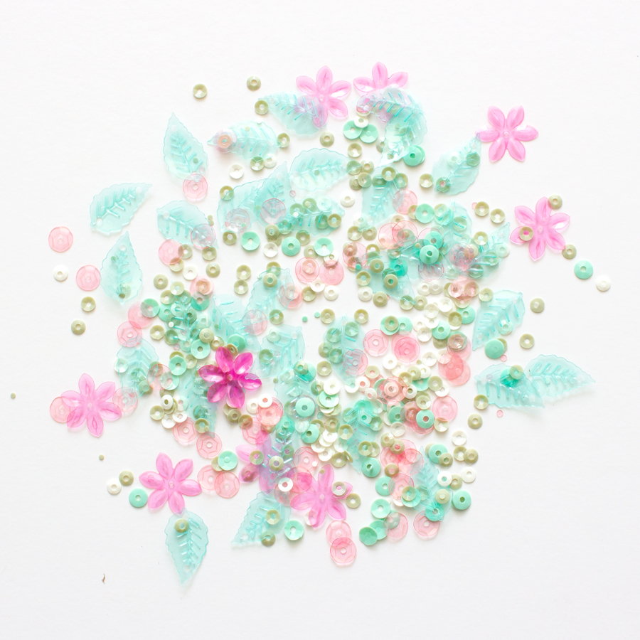 Lantejoulas coloridas em formas circulares, flores e folhas sobre fundo branco.