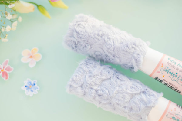 Dois rolos de fita azul claro com padrão floral em relevo sobre fundo azul e flores decorativas.