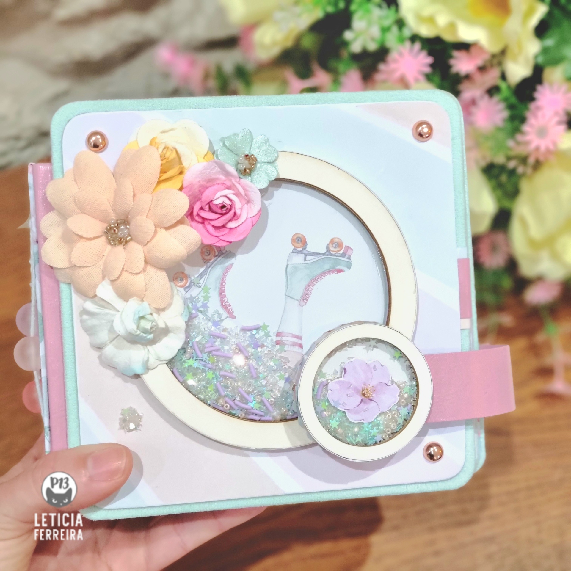 Caixa artesanal quadrada decorada com flores de tecido coloridas e purpurinas visíveis numa janela redonda.