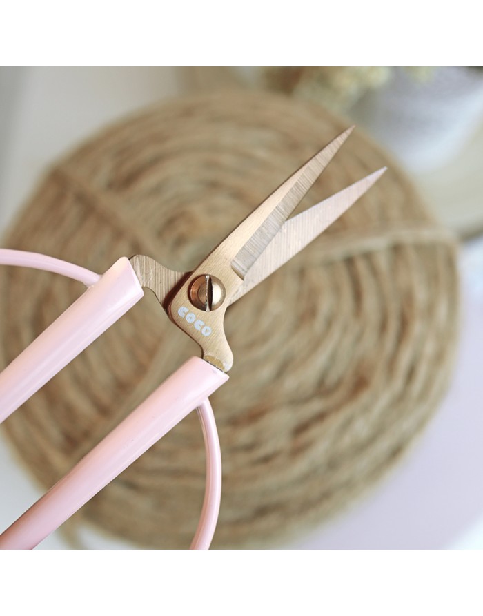 Tesoura metálica com cabo rosa claro e texto COCO próximo à articulação