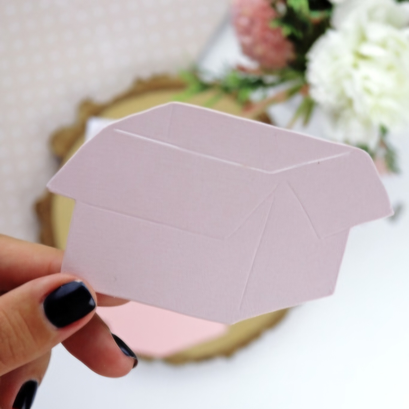 caixa de papel rosa claro sendo segurada à mão com fundo de flores desfocadas