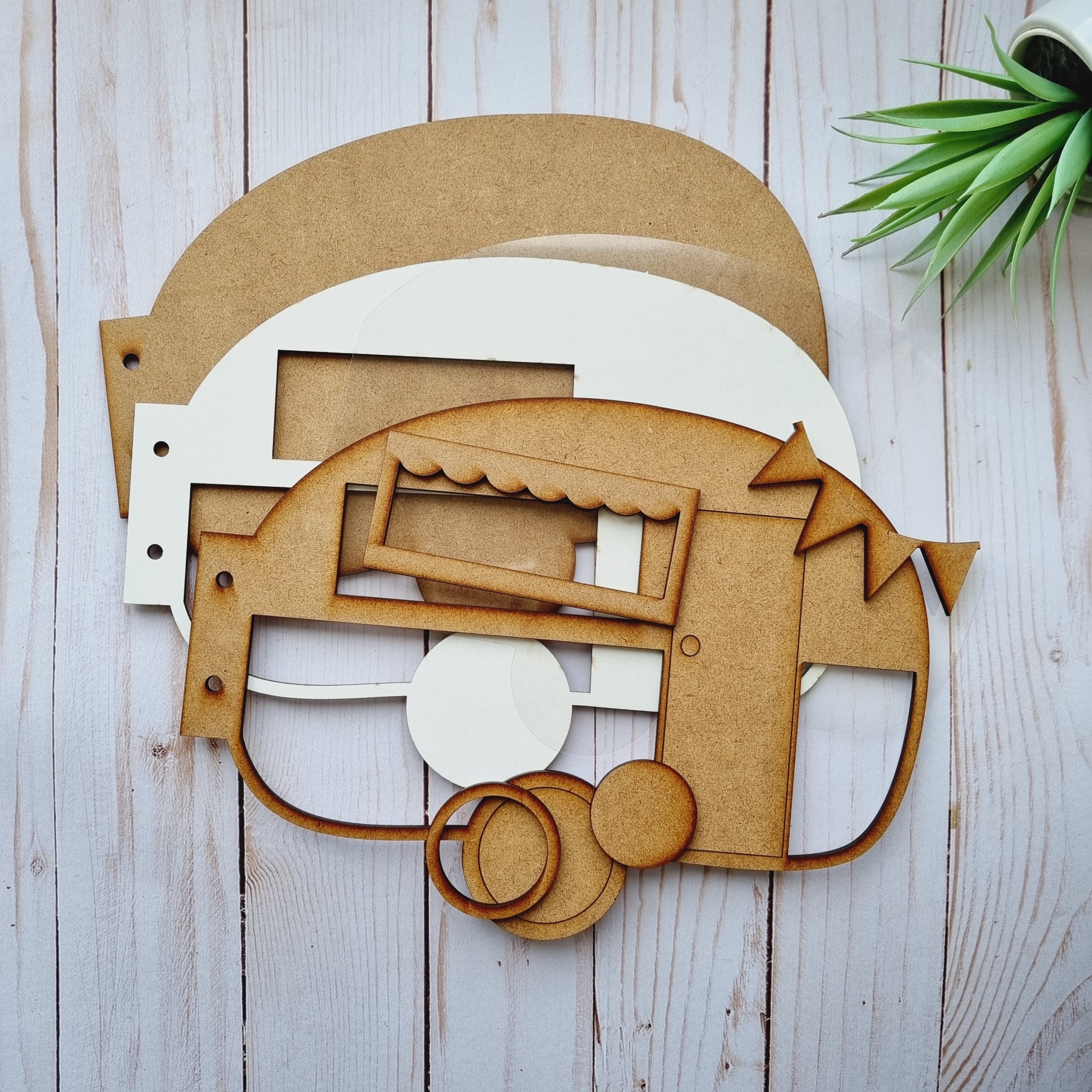 Recortes de caravana em madeira e cartão sobre fundo de madeira clara com planta verde