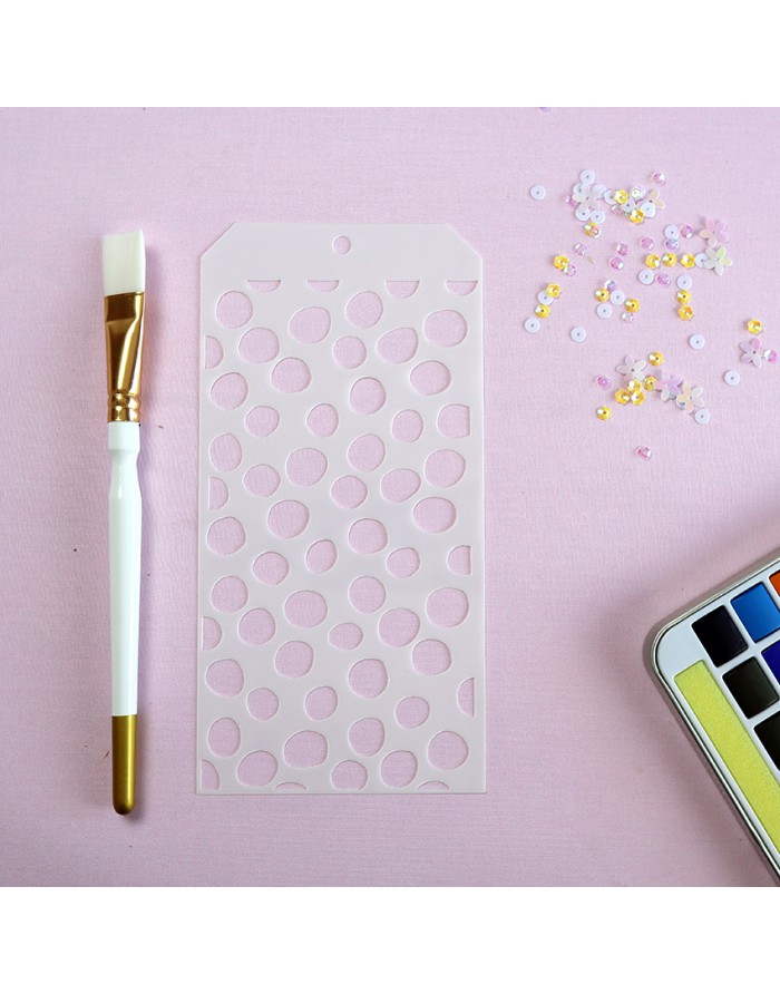 Pincel, stencil, lantejoulas e paleta de aquarela sobre fundo rosa.