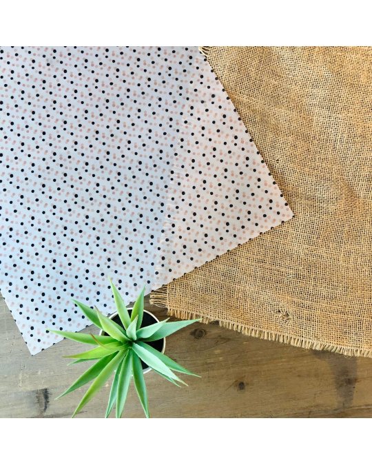 Dois tecidos, um branco com pontos pretos e um castanho rústico, sobre mesa de madeira com planta verde.
