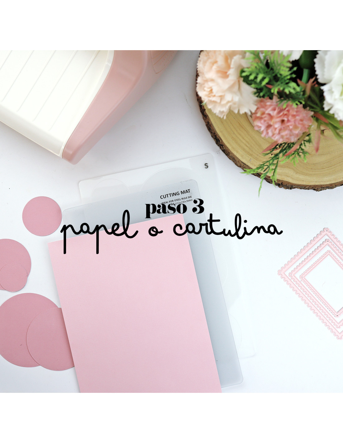 Cartolina rosa, máquina de corte e base transparente com texto em mesa branca com flores.