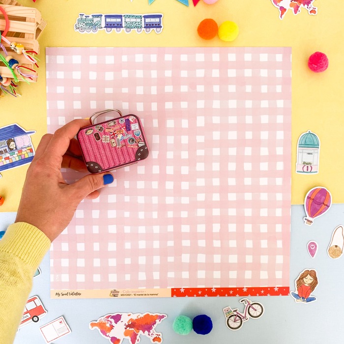 Miniatura de mala rosa com adesivos sobre pano xadrez rosa e branco com figuras recortadas ao redor