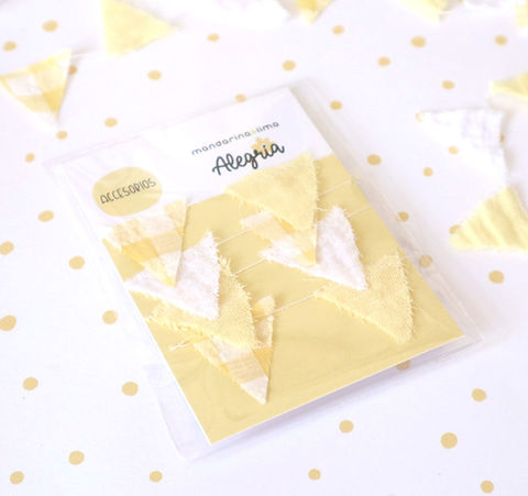 Acessórios em tecido amarelo e branco em embalagem com marca Alegria, fundo branco com pontos amarelos