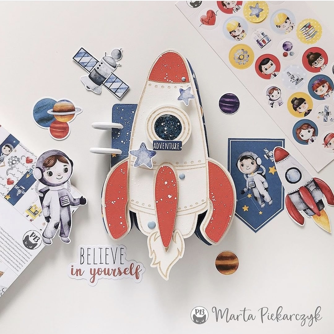 Caderno em formato de foguete e autocolantes de temas espaciais sobre fundo branco