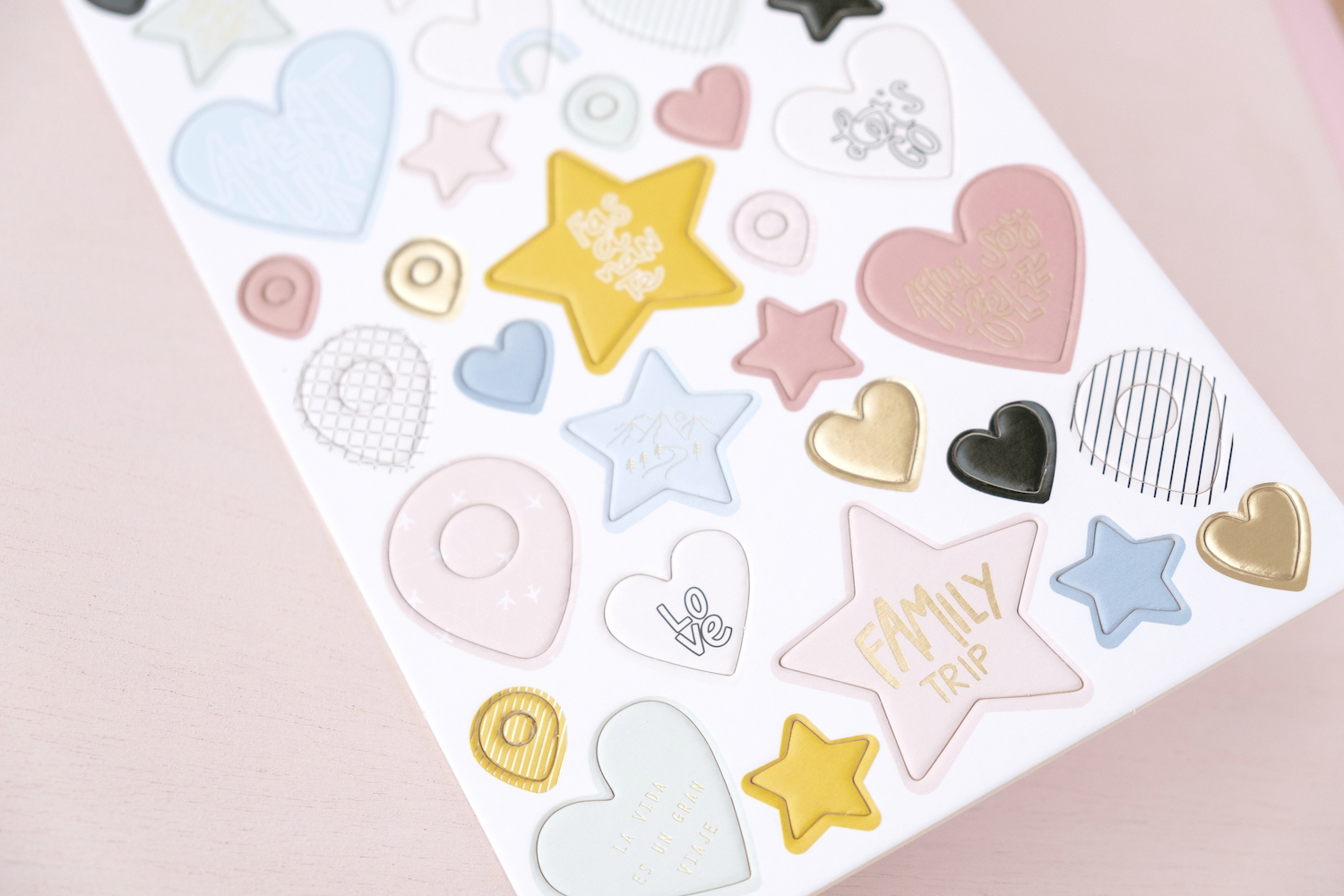 Folha de autocolantes coloridos em formas de corações, estrelas e círculos sobre fundo rosa