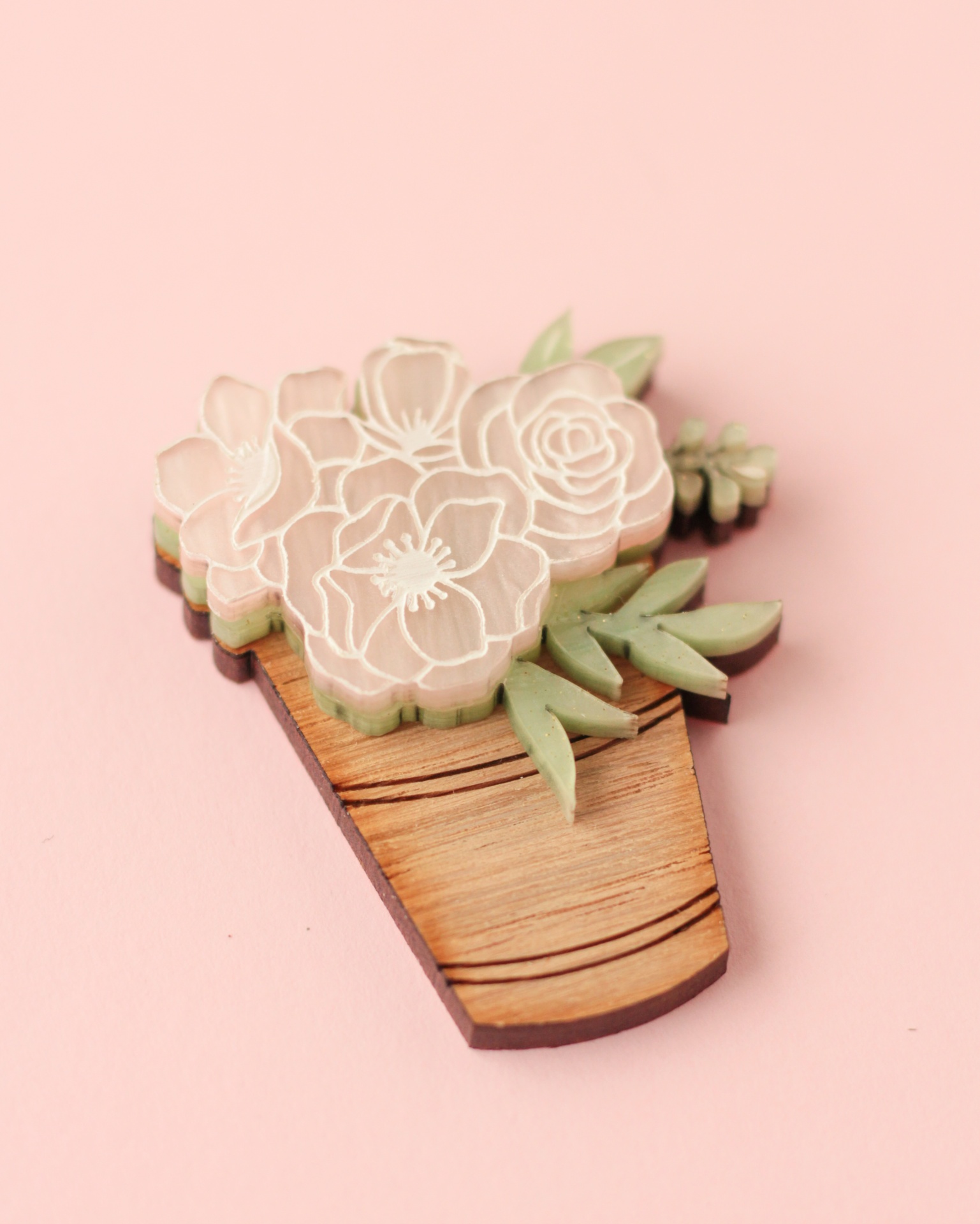 Broche de madeira em forma de vaso com flores e folhas, fundo rosa