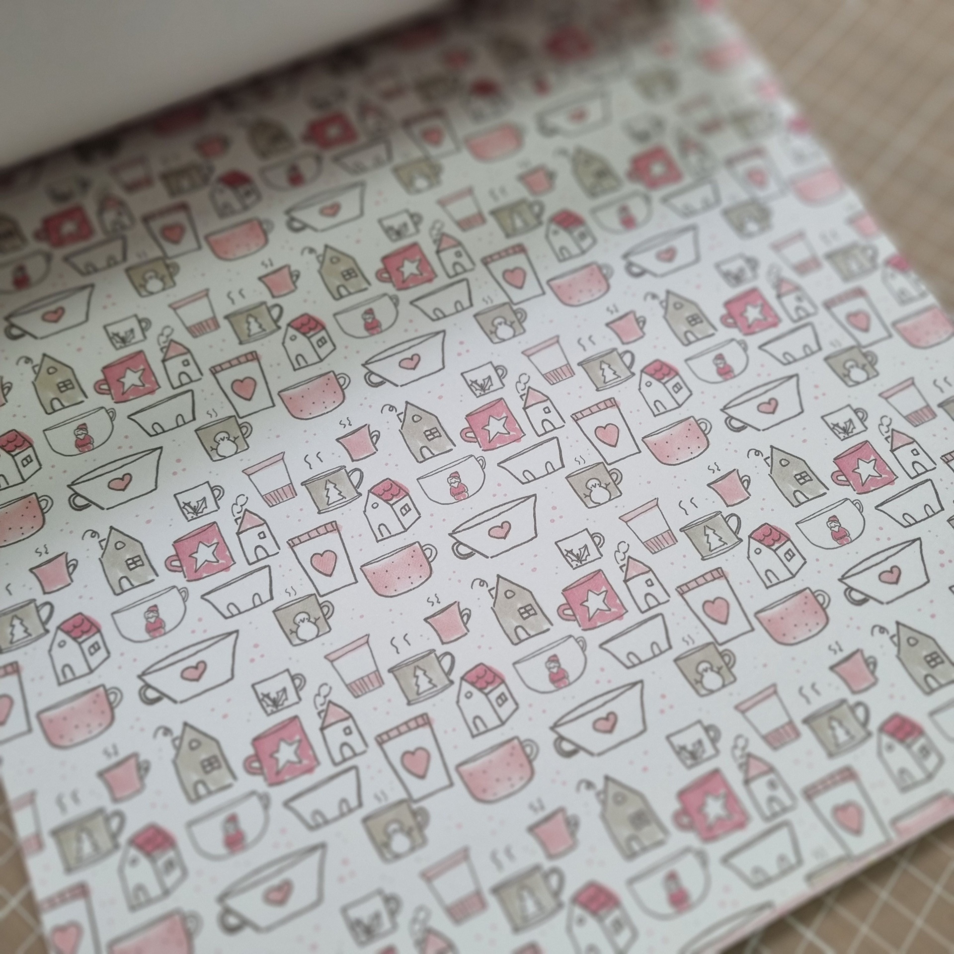 Papel com padrão de canecas, casas e bonecos de neve desenhados em rosa, vermelho e bege
