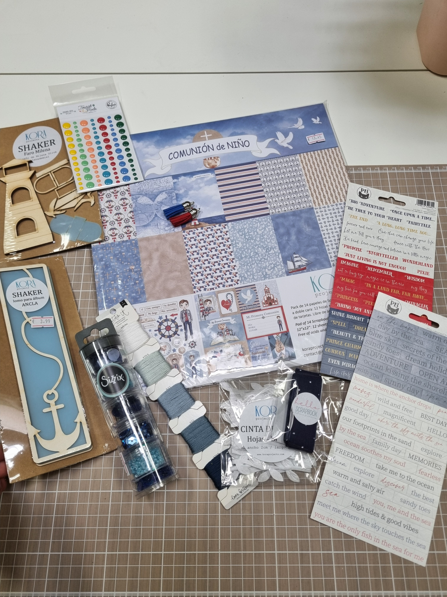 Materiais de scrapbook variados, incluindo papéis, adesivos, fitas e elementos decorativos, sobre mesa quadriculada