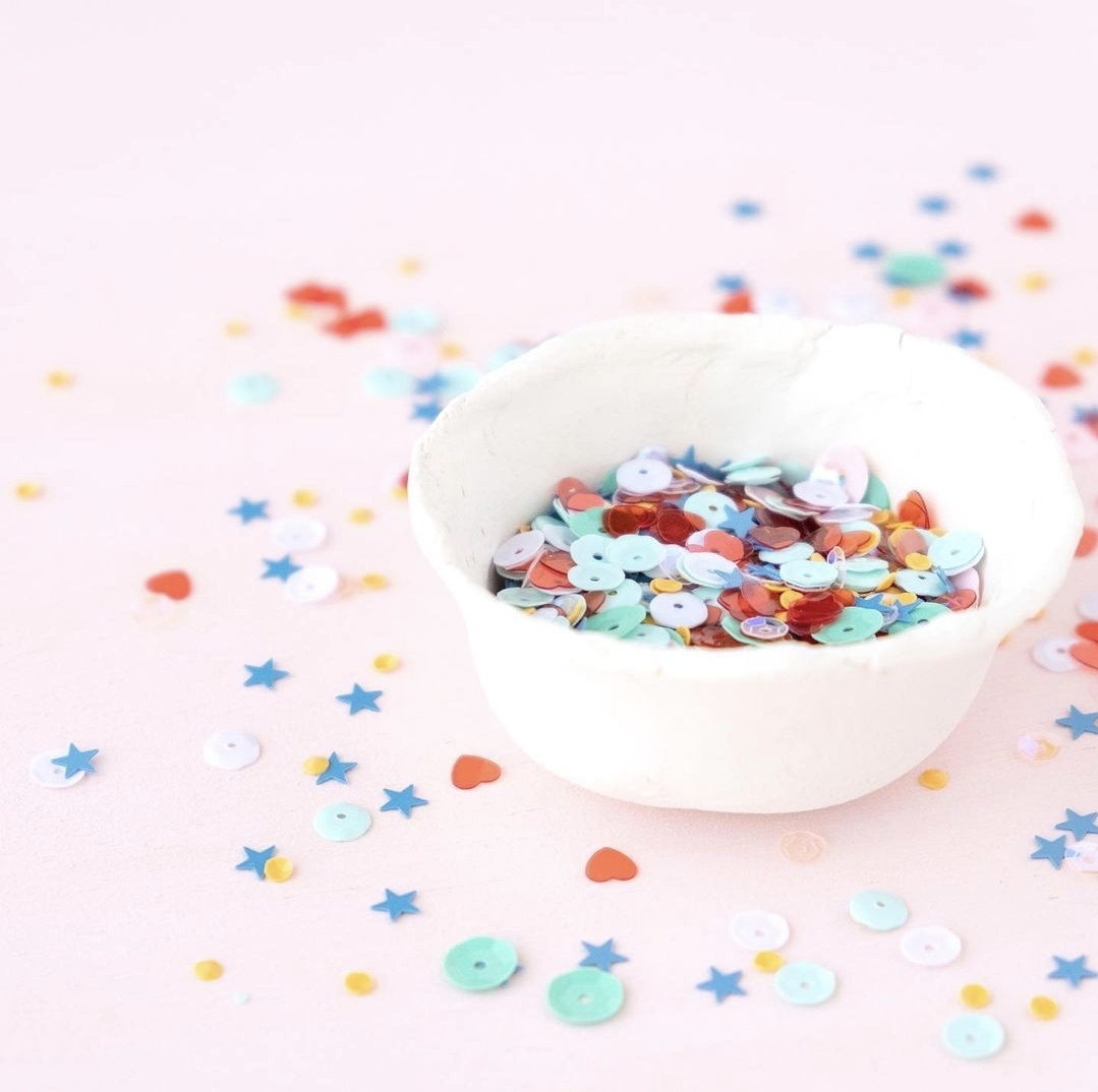 taça branca com confetes coloridos sobre superfície rosa