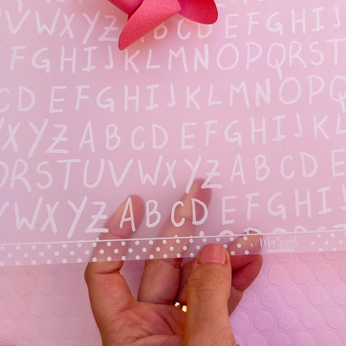 Folha plástica transparente com alfabeto branco e fita rosa com bolinhas brancas