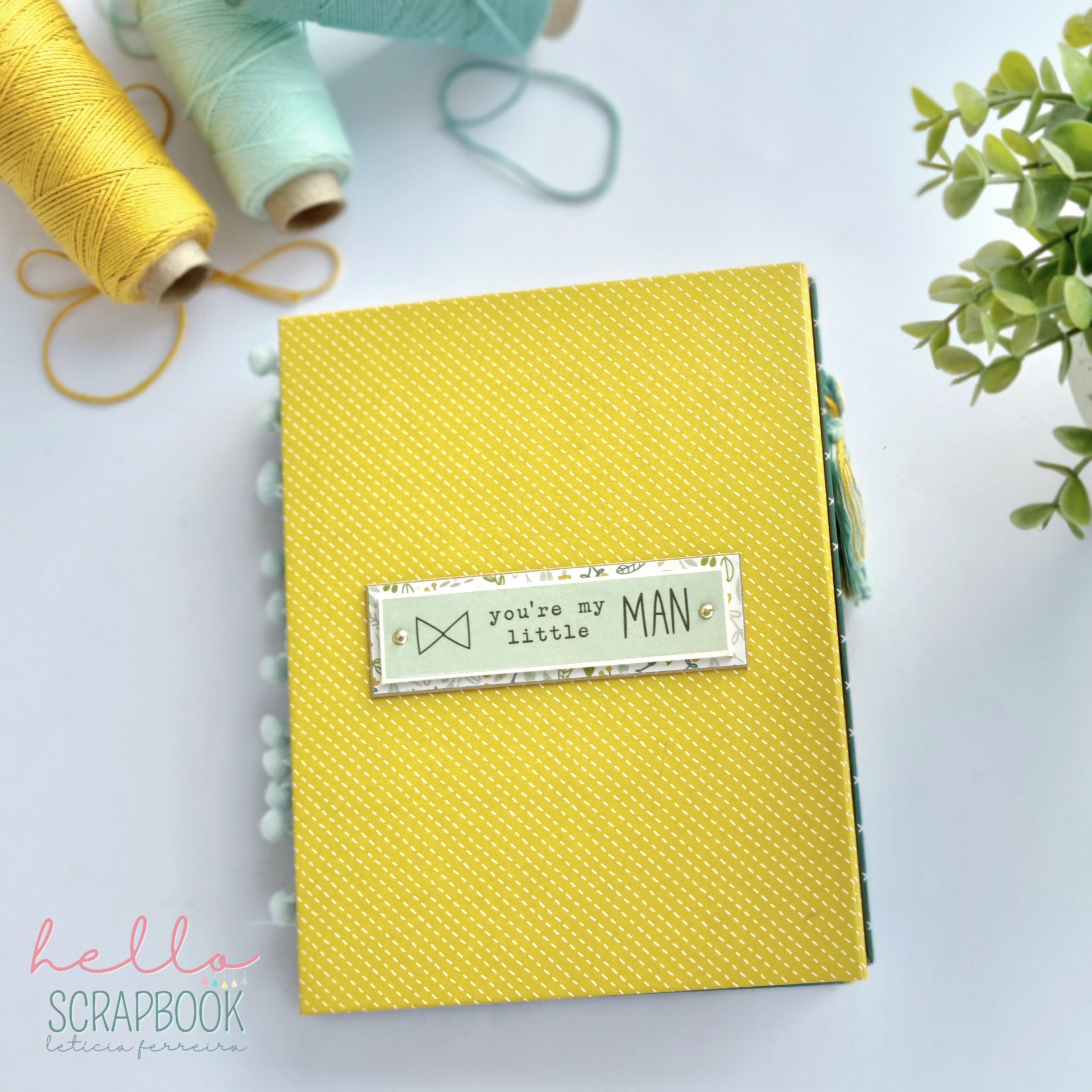 Álbum de scrapbook amarelo com etiqueta e rolos de fio coloridos ao lado