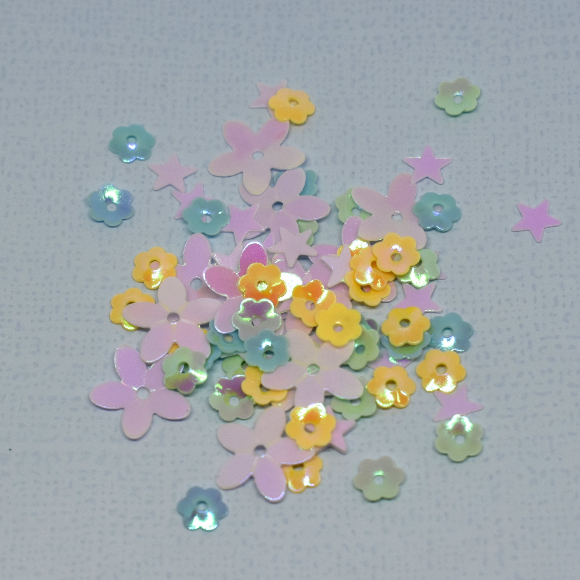 Lantejoulas coloridas em formas de flores e estrelas sobre fundo cinzento claro