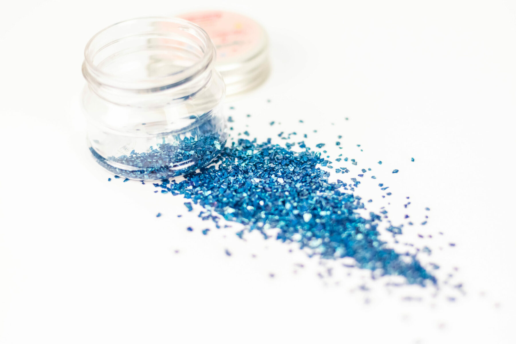 Frasco de glitter azul aberto sobre fundo branco