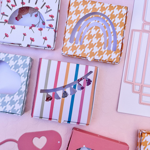 Caixas decorativas coloridas com recortes de formas diversas sobre superfície rosa