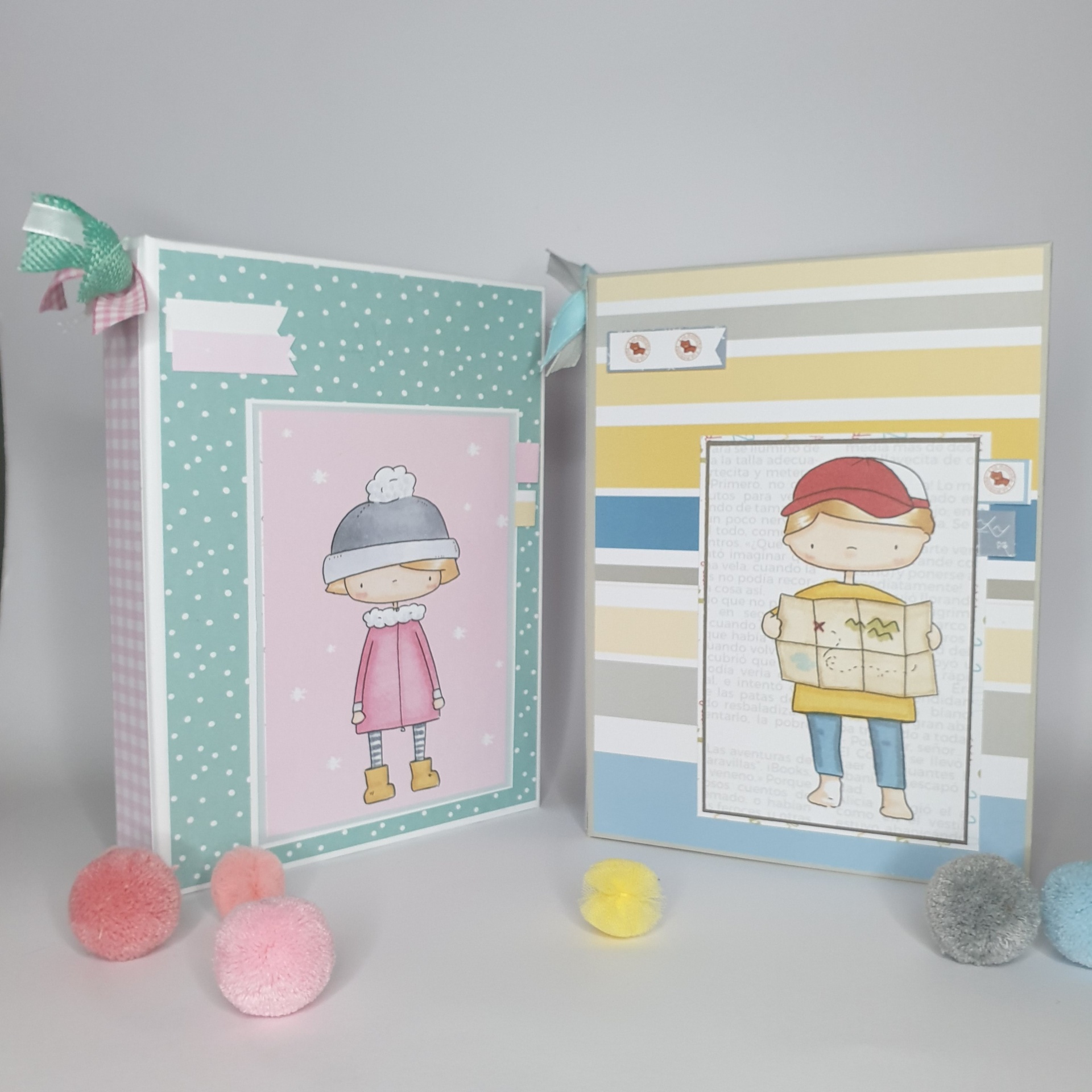 Dois álbuns decorativos com ilustrações infantis e pompons coloridos em superfície branca