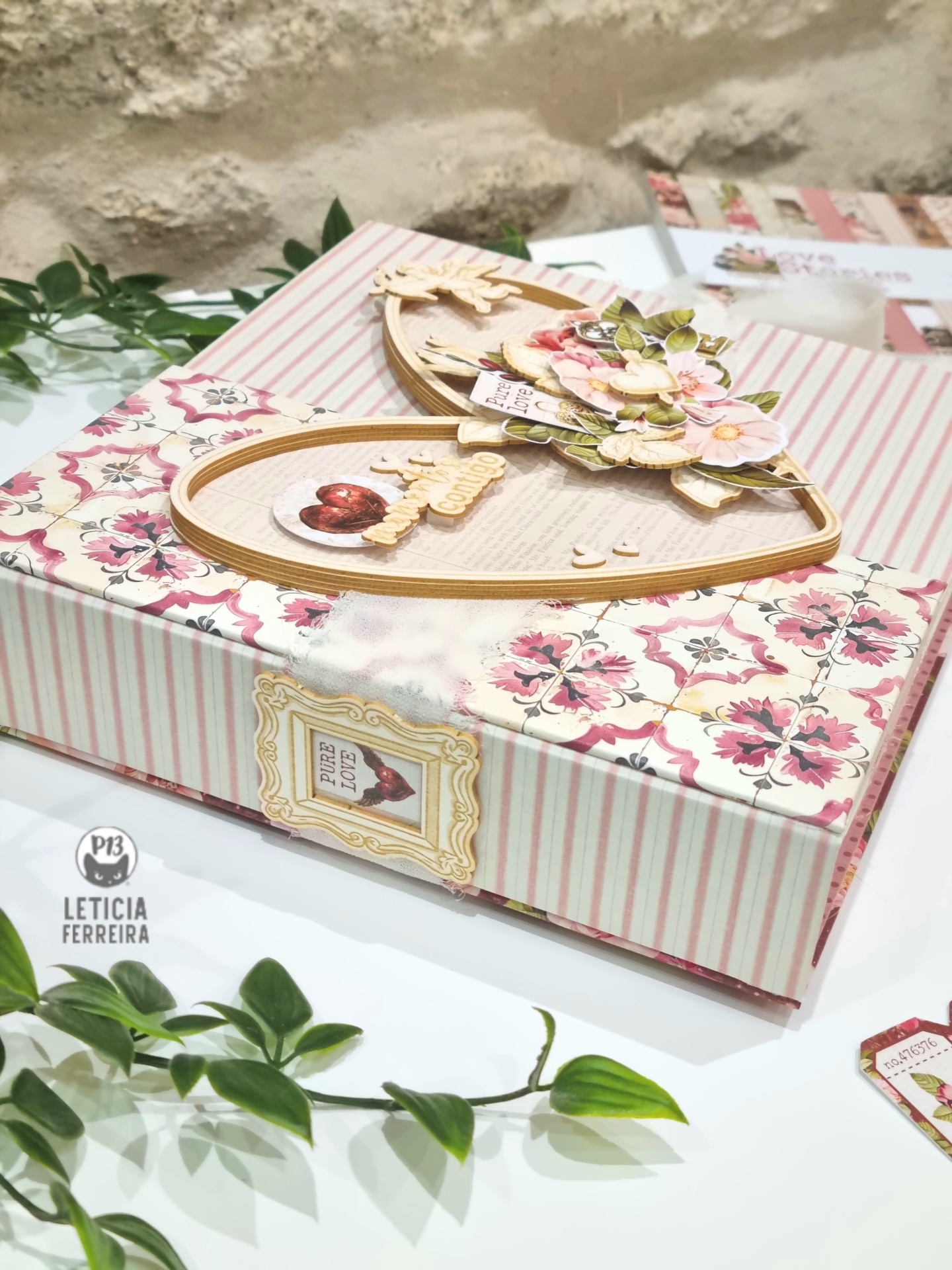 Embalagem decorativa retangular com padrão listrado rosa e flores, coração de madeira decorado e folhas verdes