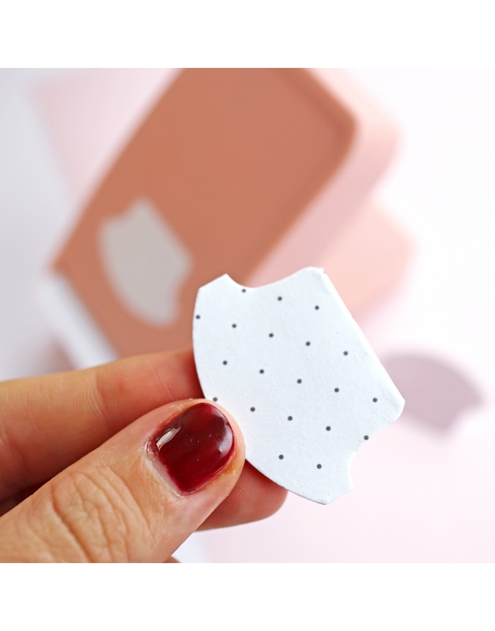 Peça branca com pontos pretos em mão com verniz vermelho, fundo desfocado cor de rosa