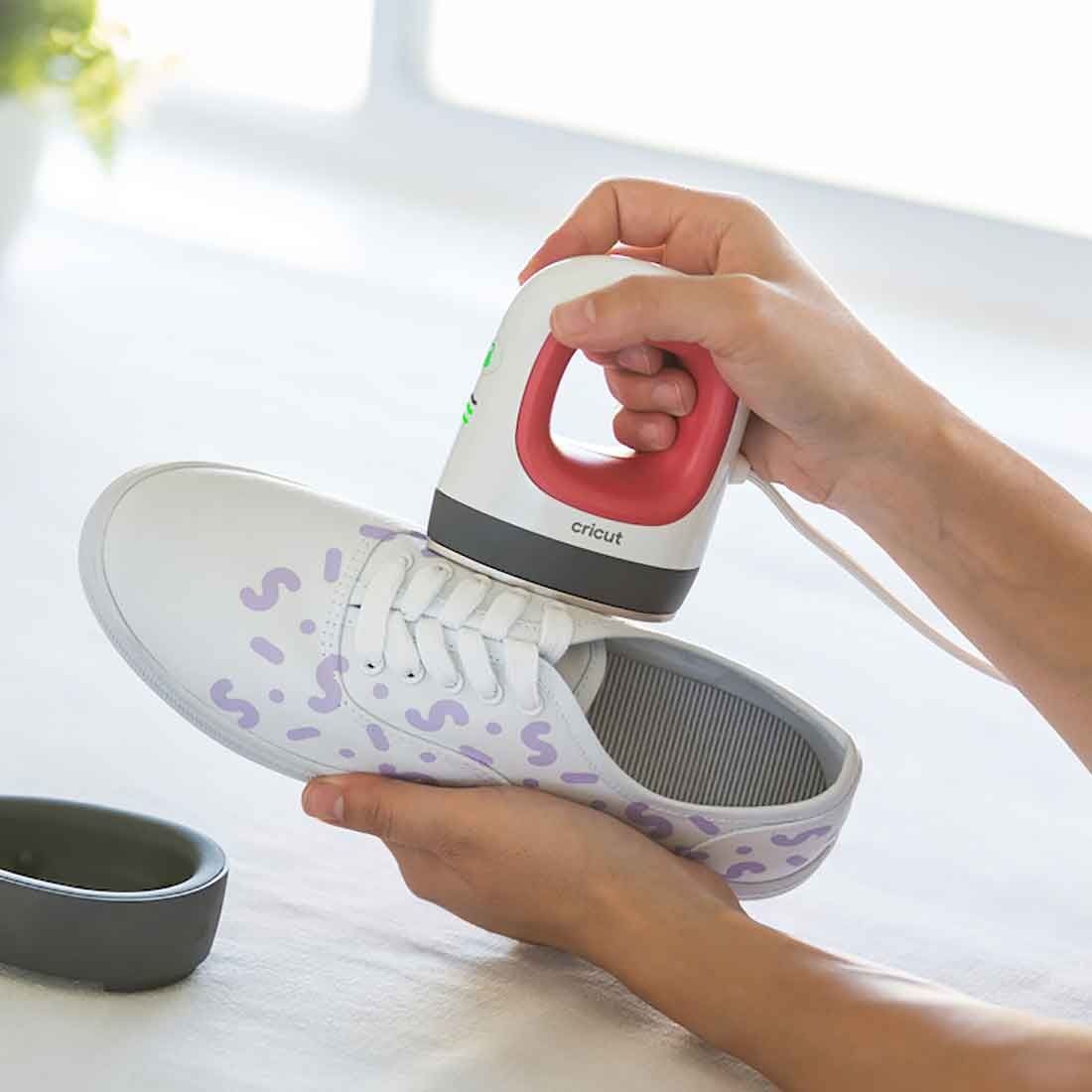 Mãos a usar ferro de engomar Cricut em sapato branco com padrões lilás