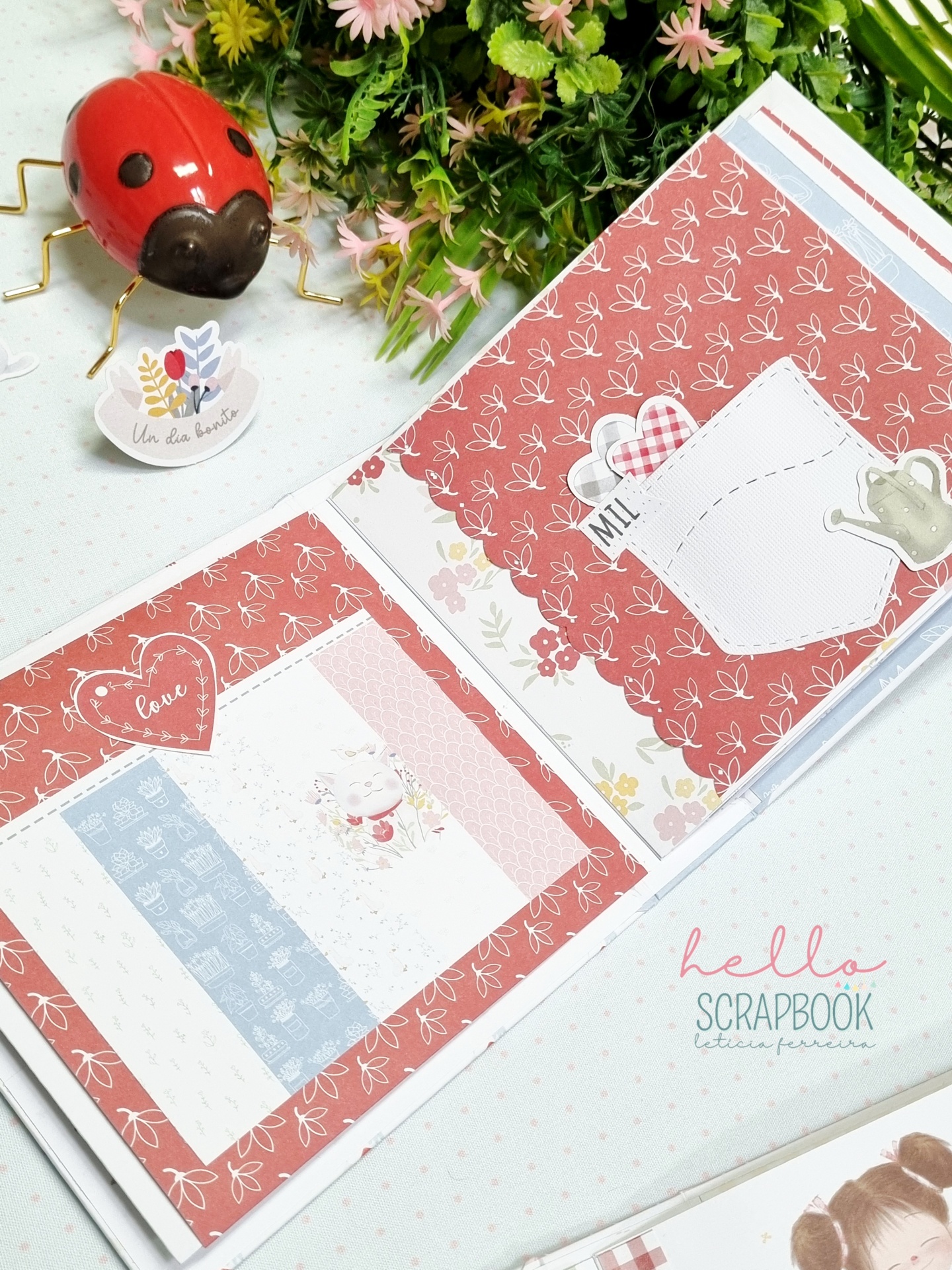 Scrapbook artesanal decorado com padrões florais e figuras em tons rosa, azul e vermelho, com joaninha decorativa ao lado.
