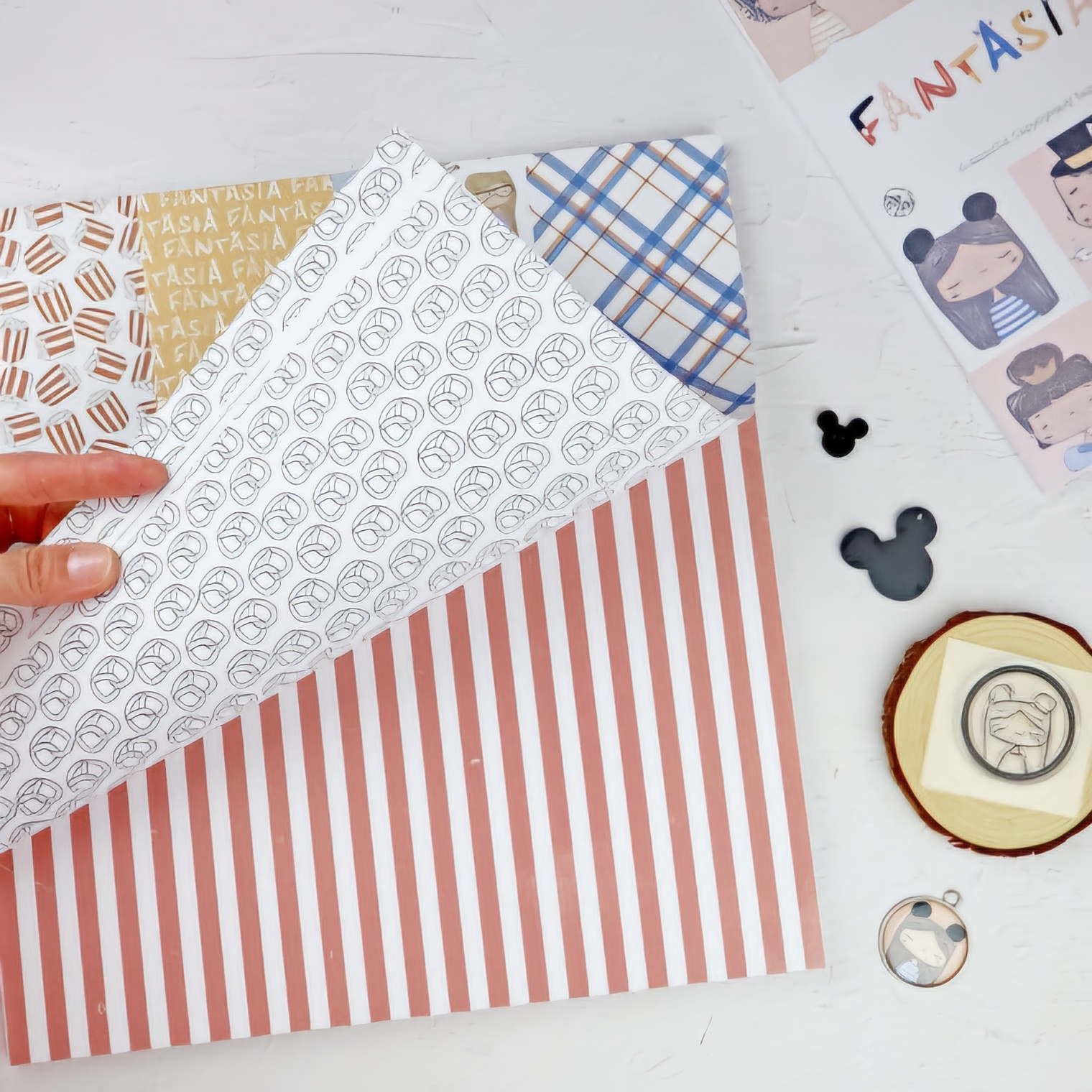 Folhas decorativas com padrões coloridos e texto Fantasia, em cima de uma mesa branca com objetos pequenos