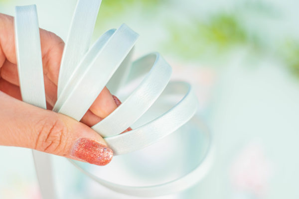 Mão segura pulseiras brancas lisas em fundo desfocado verde e branco