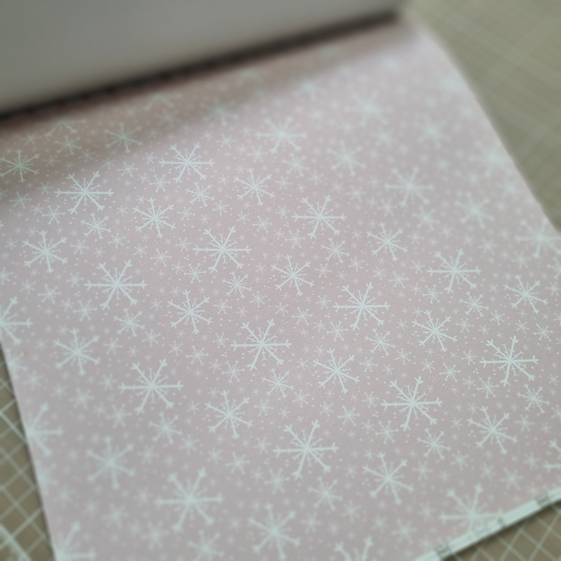 Papel rosa com flocos de neve brancos e superfície com grelha beige