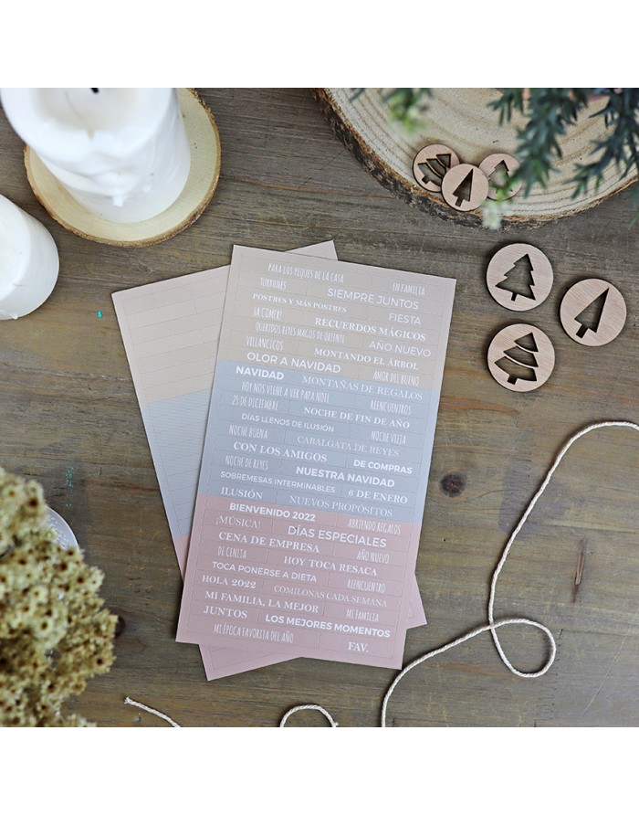 Cartões rosa com texto branco sobre mesa de madeira ao lado de círculos de madeira com símbolos de árvores, velas e corda branca.