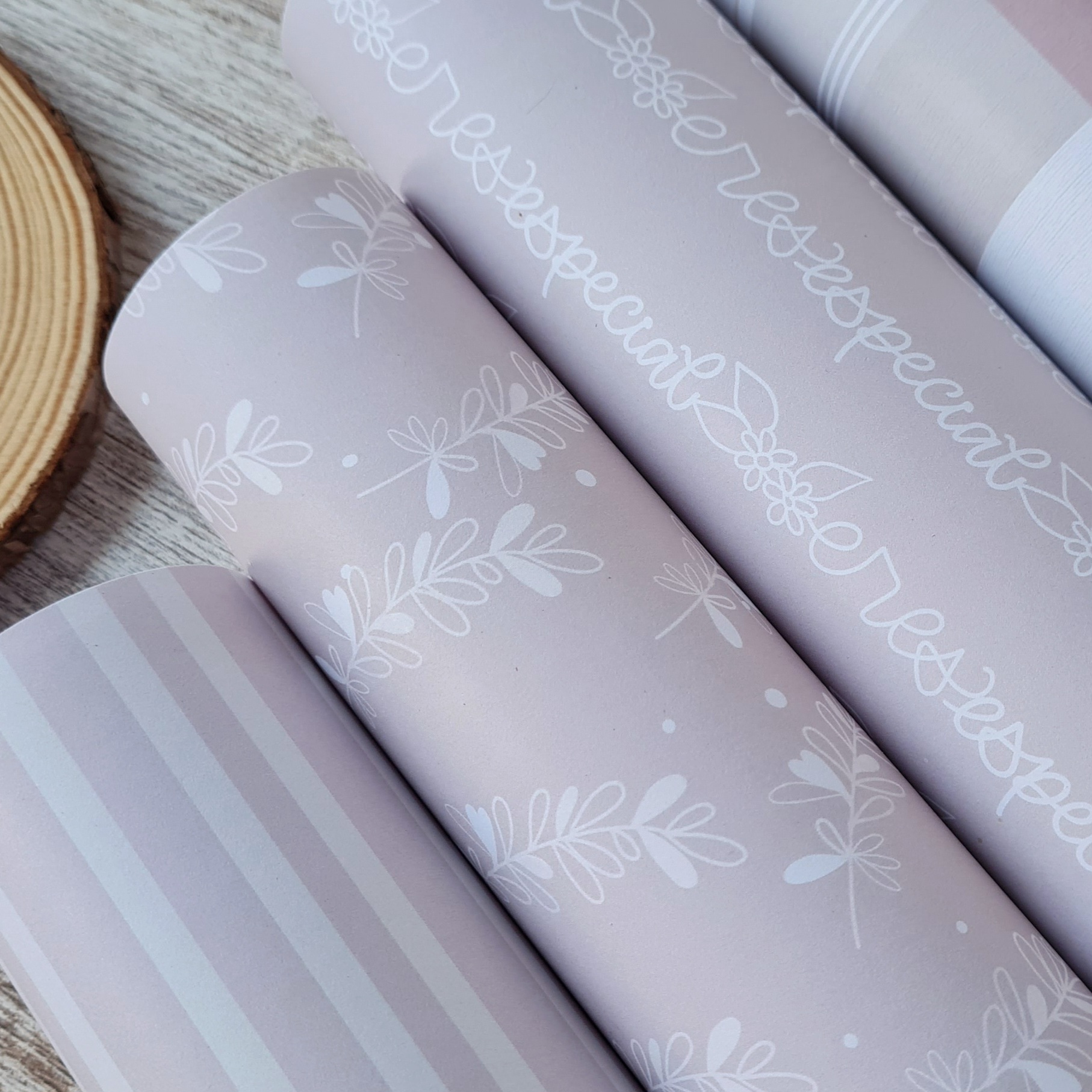 Rolos de papel decorativo lilás com padrões de riscas, folhas e texto