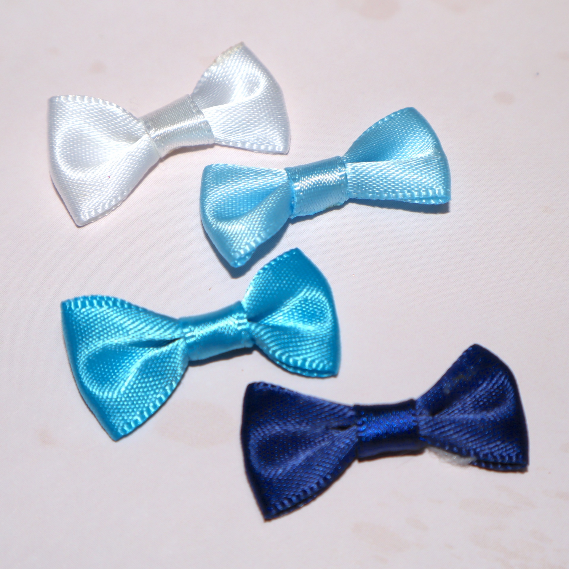 Quatro laços de cetim em tons de azul e branco sobre superfície clara