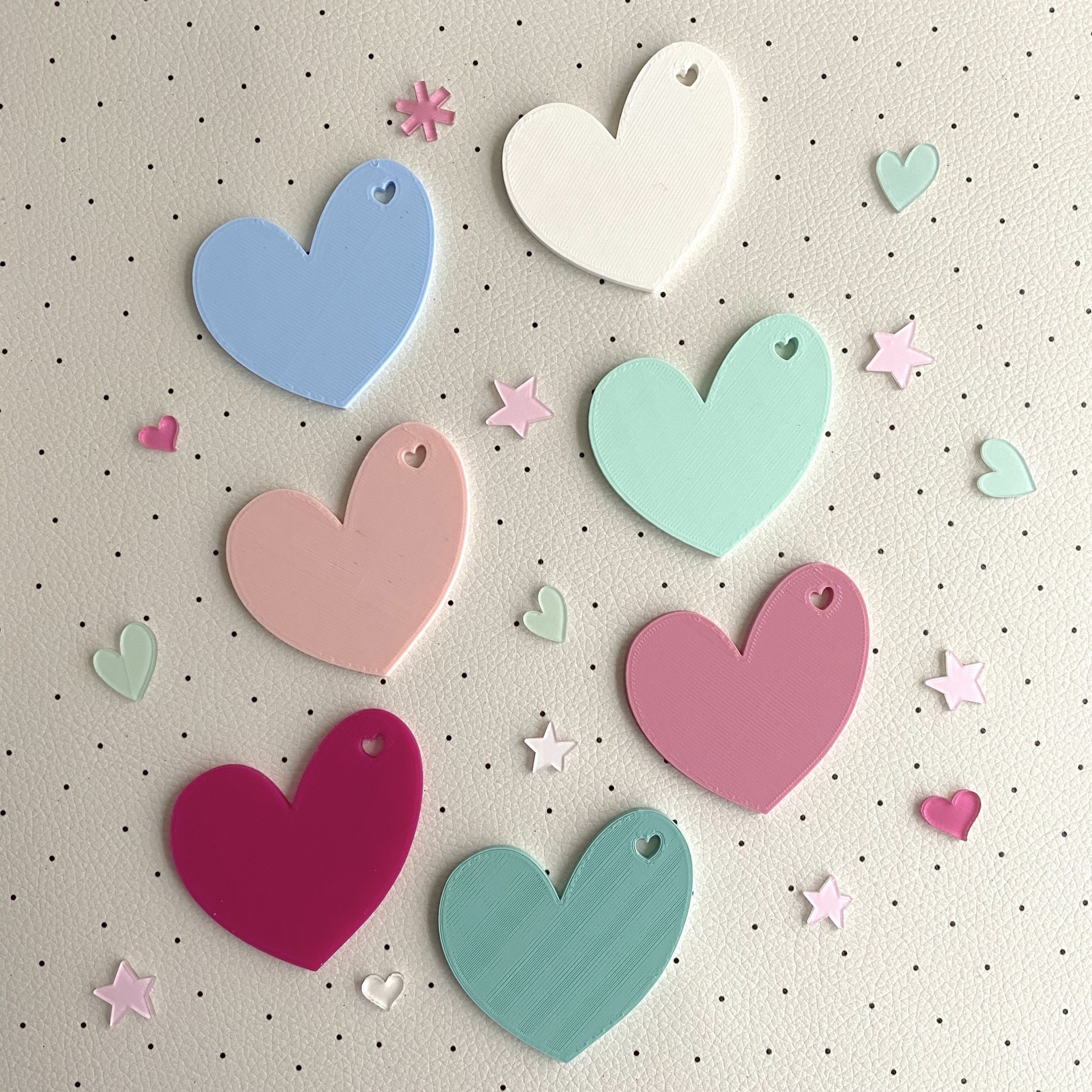 Corações coloridos de madeira com pequenos corações recortados, estrelas e corações pequenos sobre fundo bege com pontos pretos.