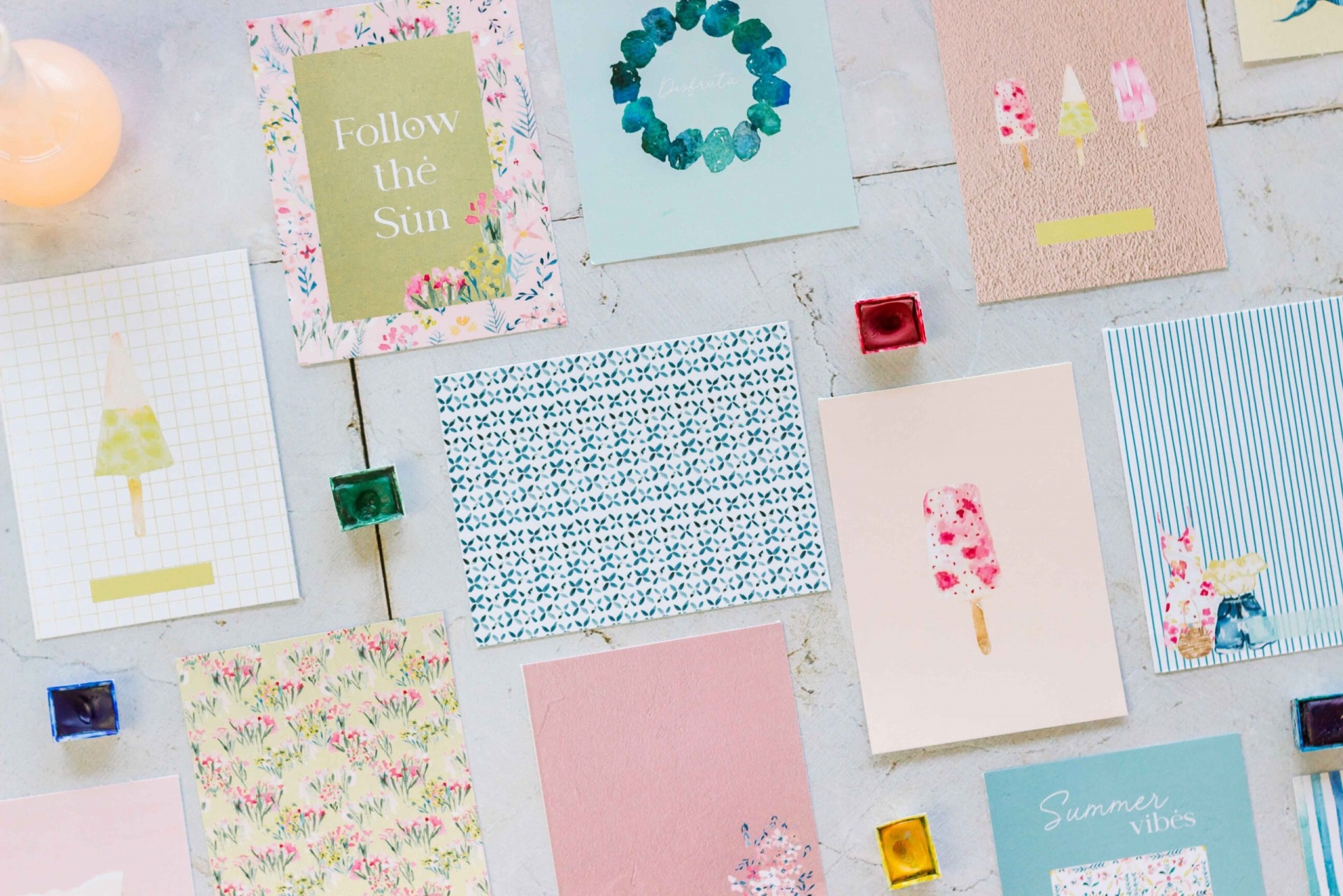 Postais coloridos com padrões florais e textos sobre superfície clara com cubos de vidro coloridos