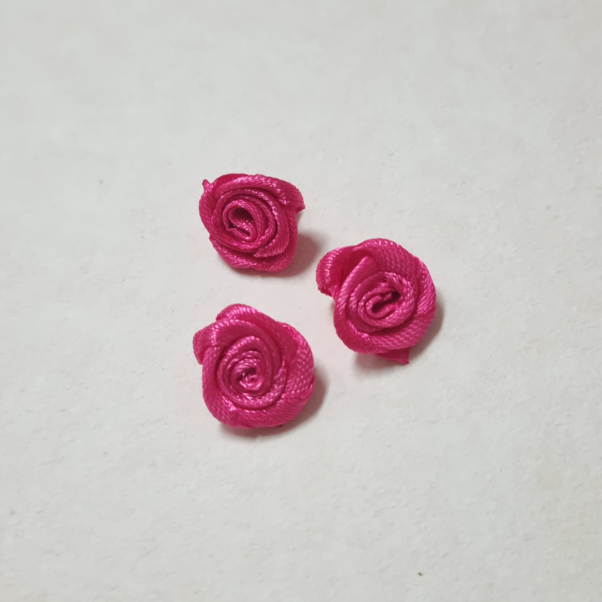 Três pequenas rosas cor-de-rosa feitas de fita decorativa sobre fundo branco