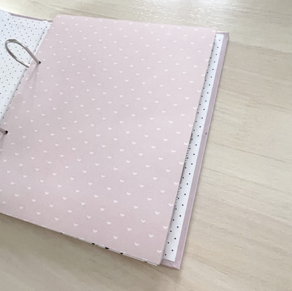 Caderno aberto com padrão de corações e pontos, sobre superfície de madeira clara