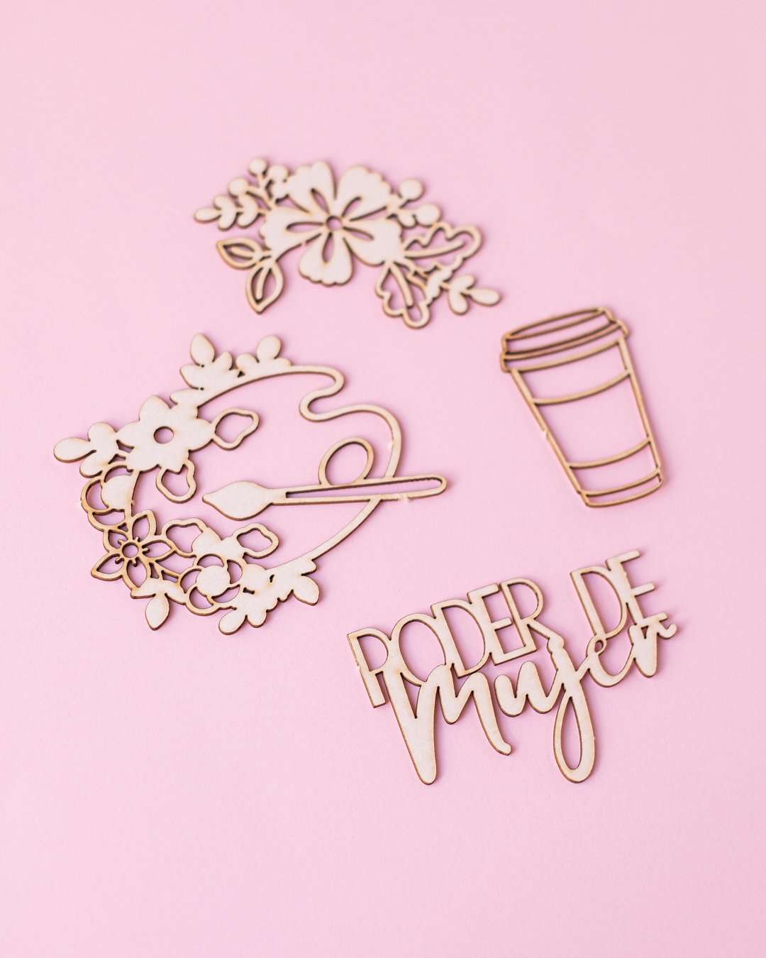 Recortes decorativos de madeira com flores, paleta, copo de café e texto em fundo rosa