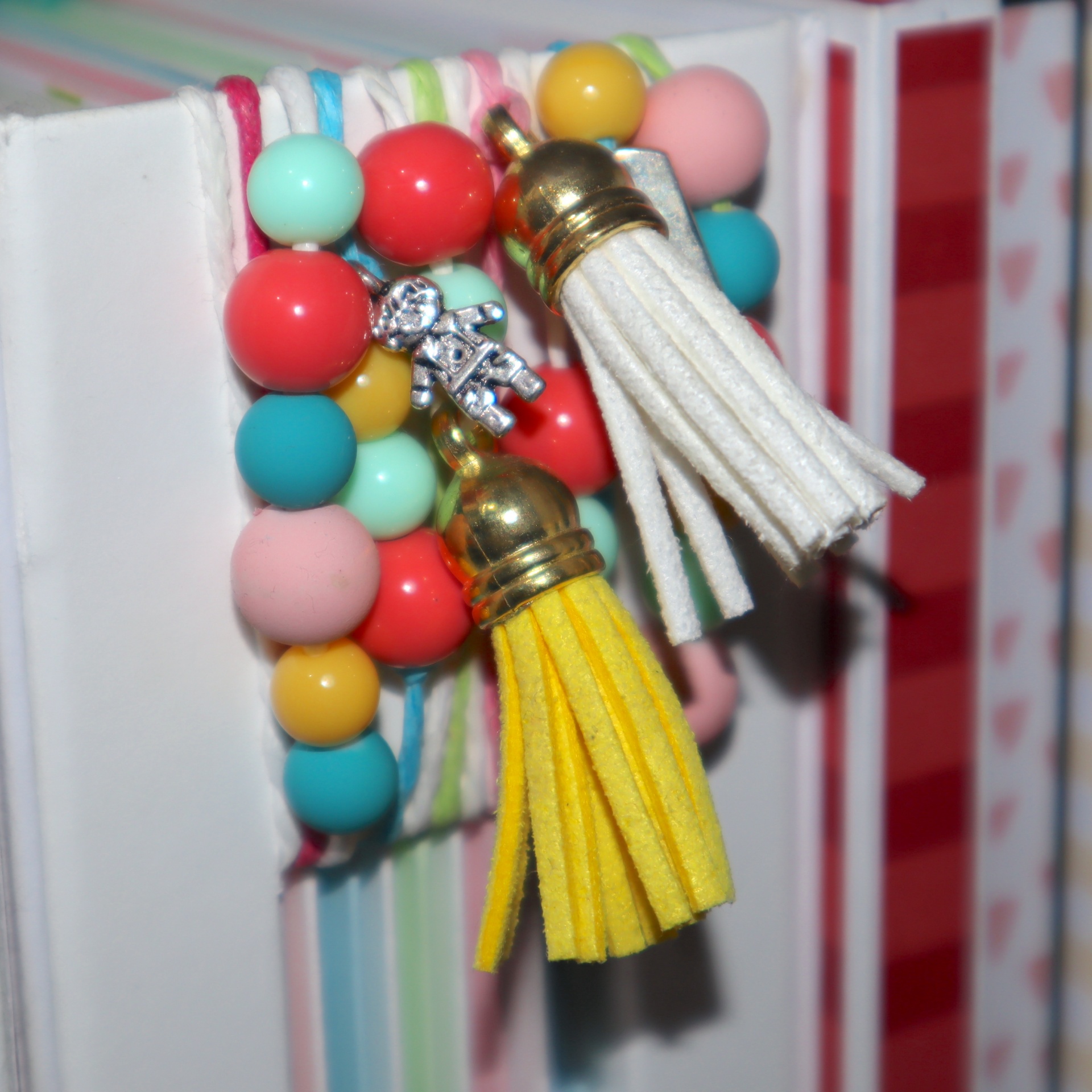 Pulseira colorida com franjas branca e amarela e pingente de boneco prateado sobre livros