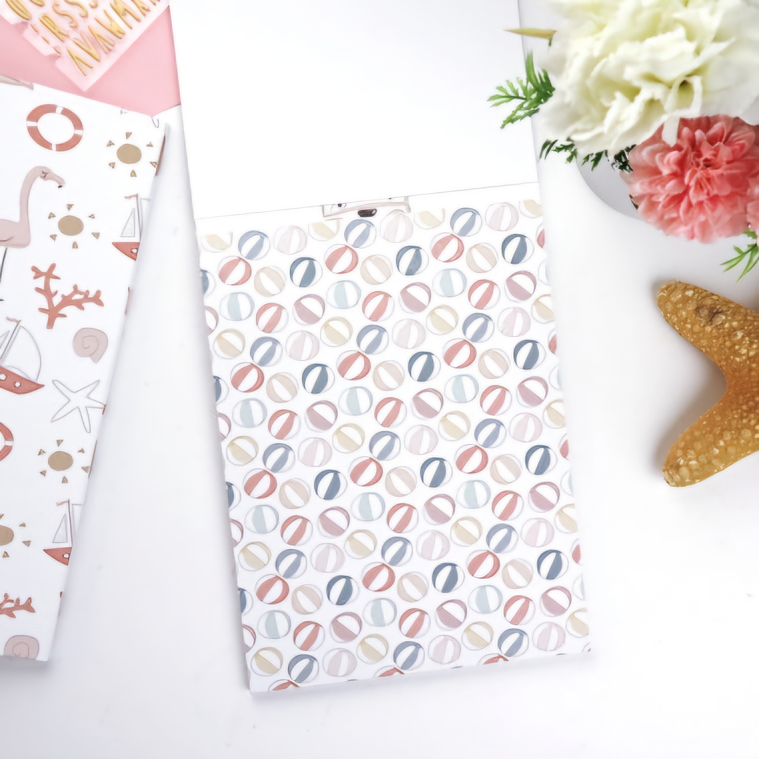 Bloco de notas com padrão colorido sobre mesa branca com flores e estrela-do-mar