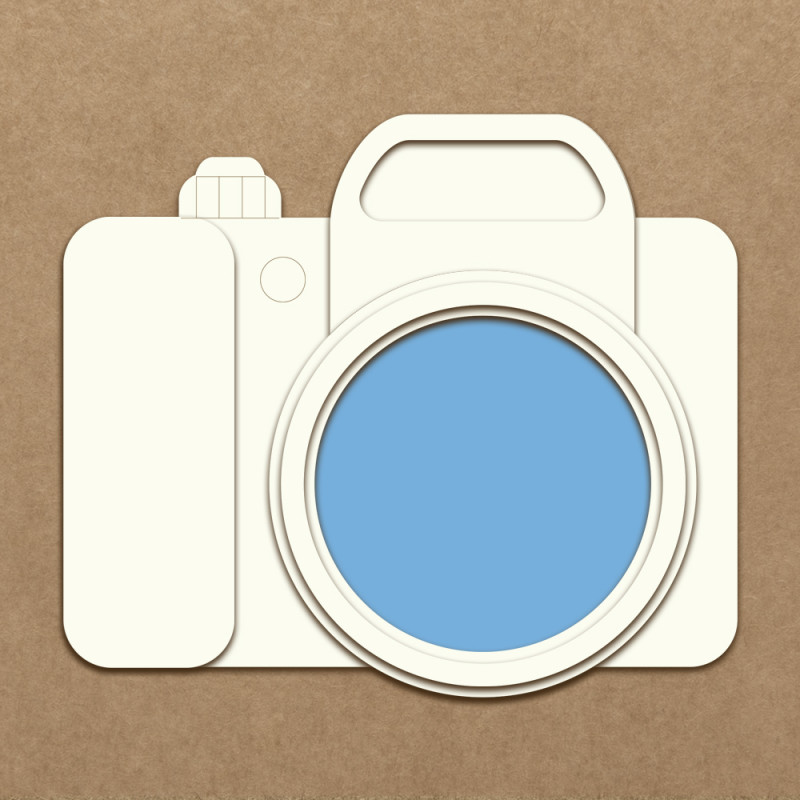 Câmara fotográfica estilizada em papel branco com lente azul sobre fundo castanho
