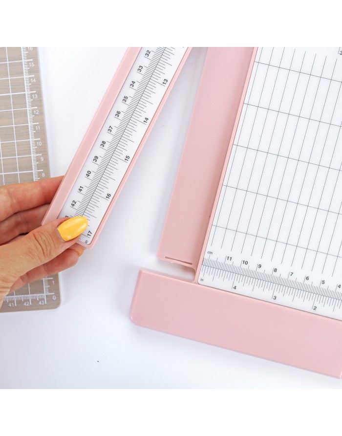 Mão segurando régua transparente sobre cortador de papel rosa