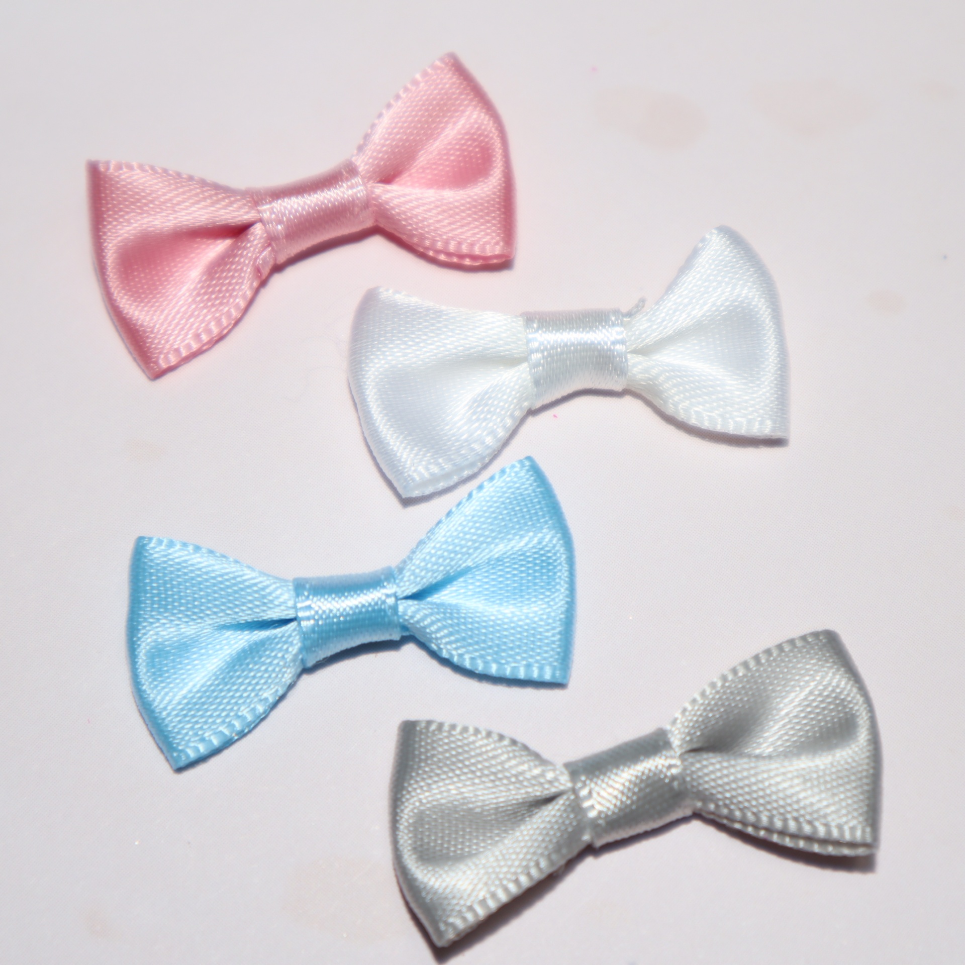 Quatro pequenos laços de cetim em diferentes cores sobre fundo branco