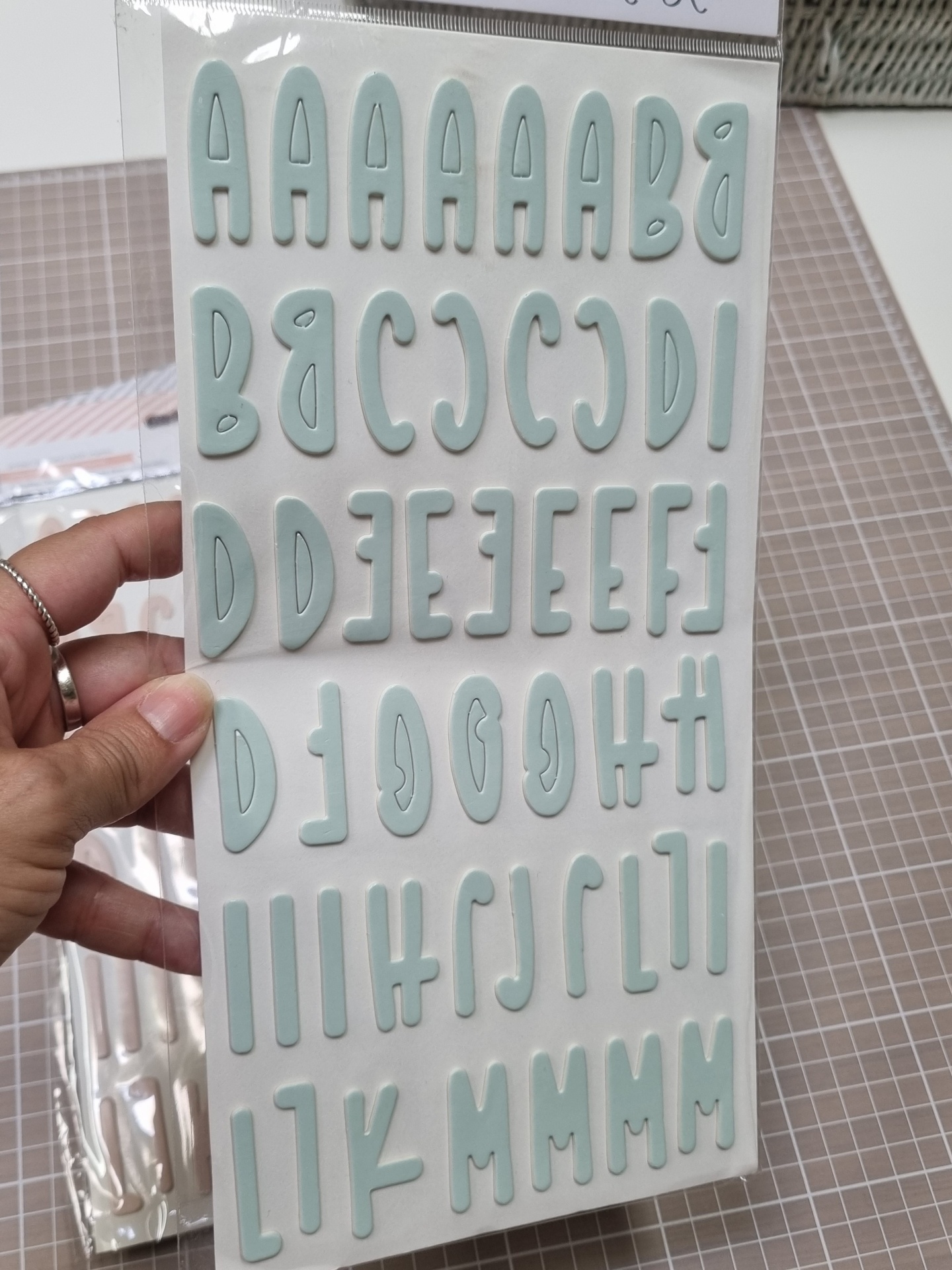 Folha de autocolantes em forma de letras maiúsculas azul esverdeadas em relevo numa embalagem plástica