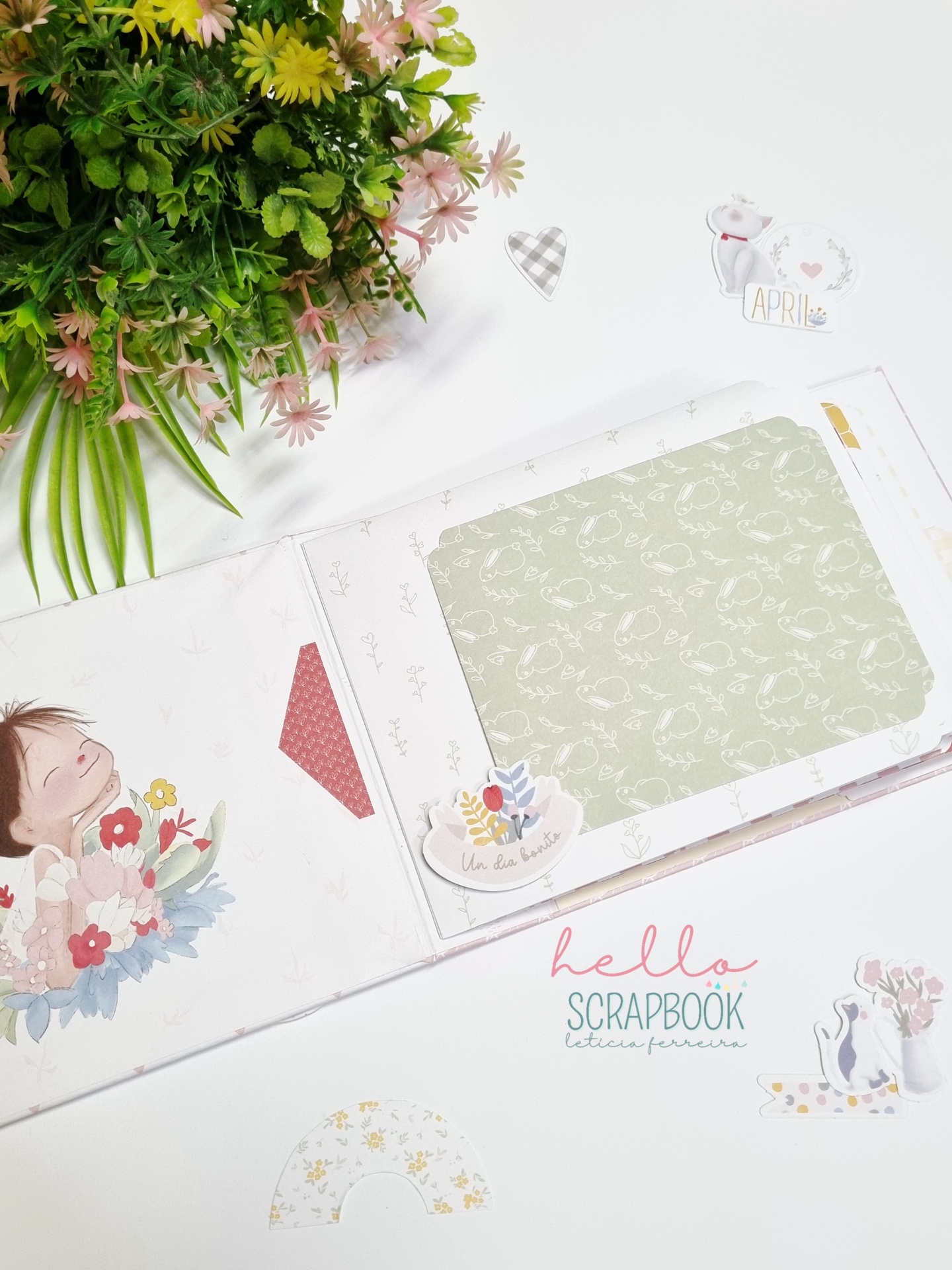 Livro de scrapbook decorado com ilustrações e flores, com plantas verdes ao lado