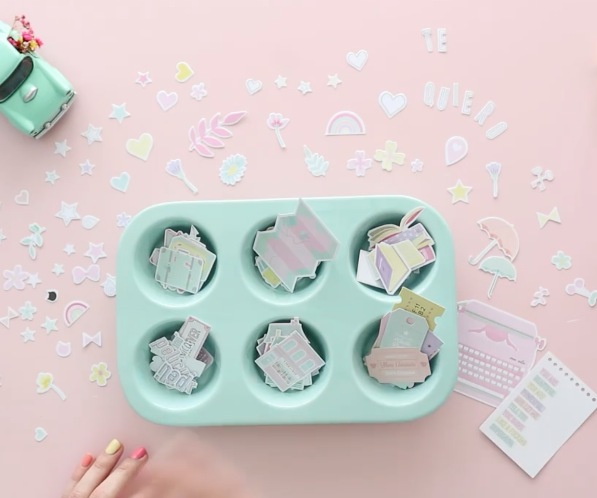 Conjunto de recipientes azuis claros com papéis recortados e adesivos decorativos coloridos sobre superfície rosa