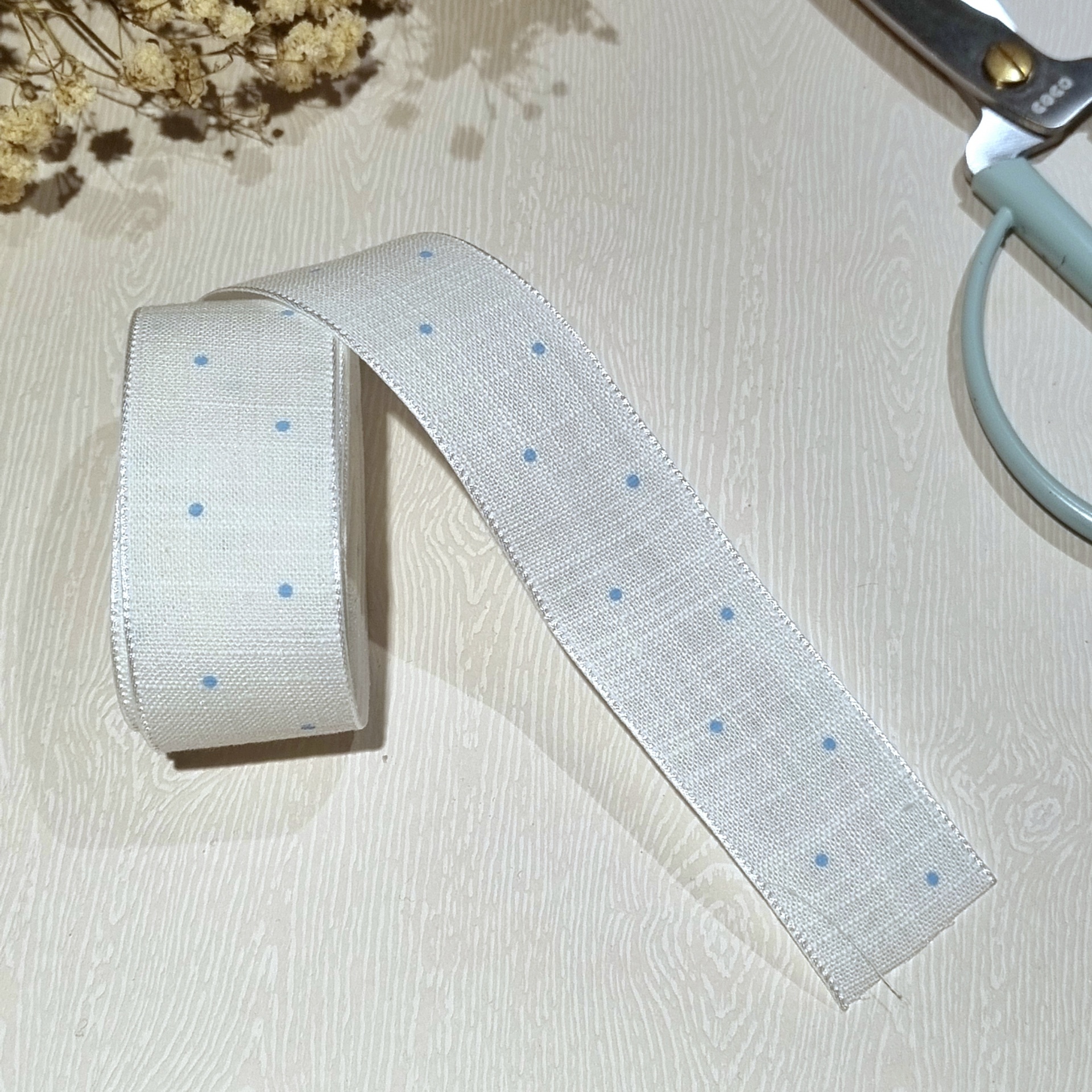 Fita decorativa branca com pontos azuis sobre superfície clara ao lado de tesoura