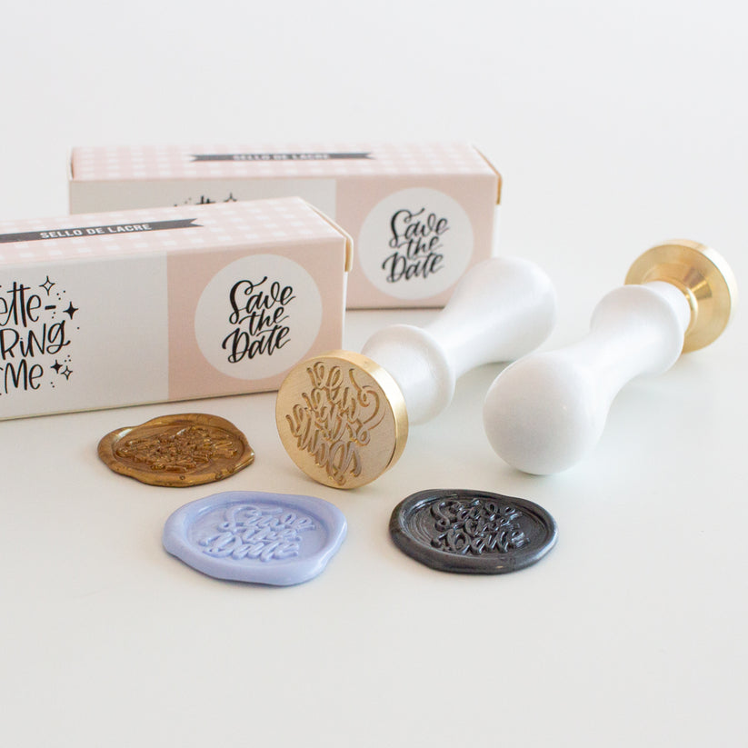 Carimbos de lacre com selos florais e cera em várias cores ao lado de caixas cor de rosa com etiqueta 'Save the Date'.