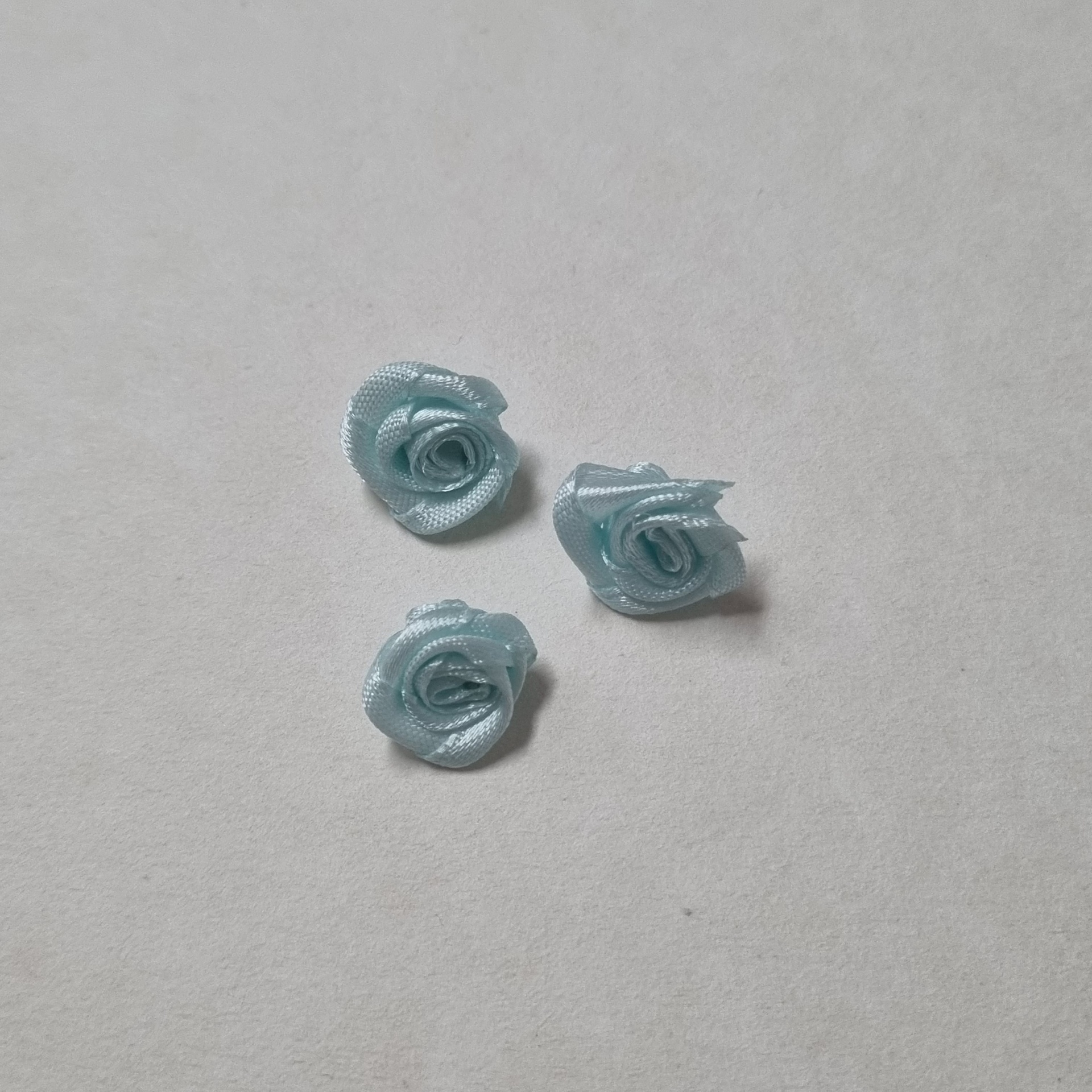 Três flores cor-de-azul claras feitas em fita de cetim sobre superfície branca